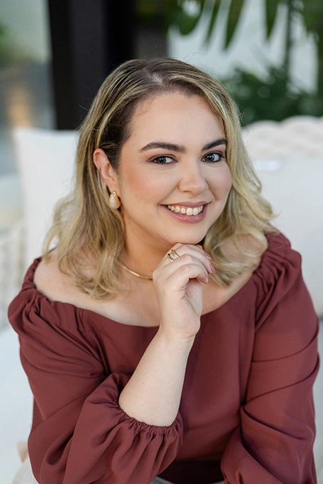 Foto da Ana Carolina sorrindo com a mão levemente apoiada no queixo